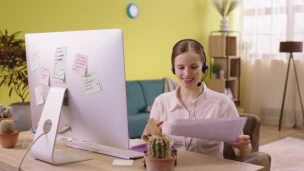 Работая из дома онлайн красивая женщина архитектор анализируя свои заметки и планы на работу она носит гарнитуру и улыбается мило — стоковое видео