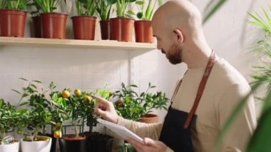 Çiçekçi dükkanındaki yakışıklı adam kameranın önünde dizüstü bilgisayarına notlar yazıyor.