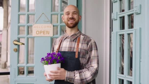 Koncepcja małego biznesu kwiaciarnia przedsiębiorca charyzmatyczny człowiek właściciel kwiaciarni uśmiechając się duży do aparatu i trzymając doniczkę kwiatów w rękach — Wideo stockowe