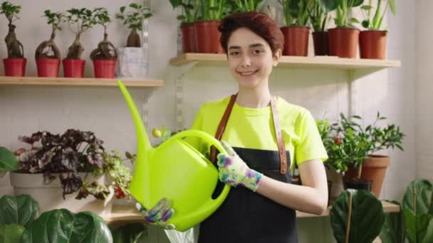 Beautiful florist lady posing in front of the camera with a watering can she smiling cute in the middle of floral store — Vídeos de Stock