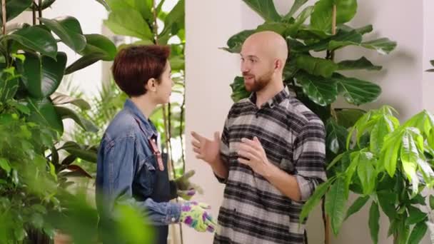 Glad kund vit ser kille och söt dam florist kvinna tillsammans diskuterar om växterna int he växthus — Stockvideo