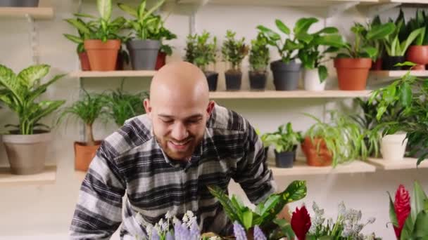 Good looking man customer at the floral shop happy with a large smile smelling the flowers from the shop shelves he wants to choose one of the plant to buy — Vídeo de Stock