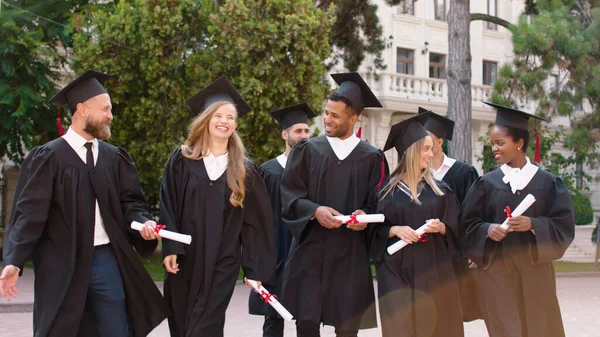 Walking in front of the camera graduates students multiracial and their professor charismatic man after the graduation they discussing and feeling excited — Foto Stock
