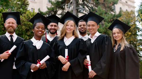 Carismatico e bello giovani laureati studenti primo piano per la fotocamera in posa dopo la laurea in possesso di diplomi nel giardino del college — Foto Stock