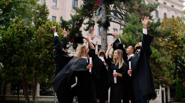 Groupe multiethnique d'étudiants diplômés après la remise des diplômes dans le parc du collège a vomi les casquettes de remise des diplômes très excité et détenant les diplômes — Photo