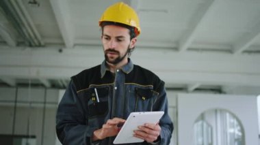 İnşaat alanı, kameranın önünde yürüyor ve dijital tablete bakıyor. Özel üniformalı ve kasklı bir iş adamının planını inceliyor.