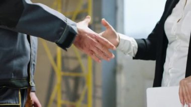 Closeup taking video details of a businesswoman shaking hands with a constructor worker at construction site