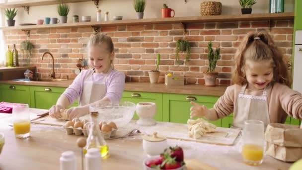 在厨房的岛上，两个可爱的小女孩在玩着面团，一边笑着，一边兴奋地把面粉吹向对方 — 图库视频影像