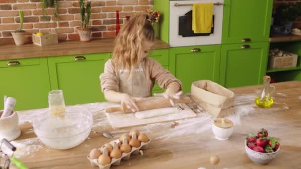 At luminous amazing rustic kitchen a cute girl preparing her favourite dessert she using the kitchen roller for dough and take some flour add over the dough at the kitchen island — Stockvideo