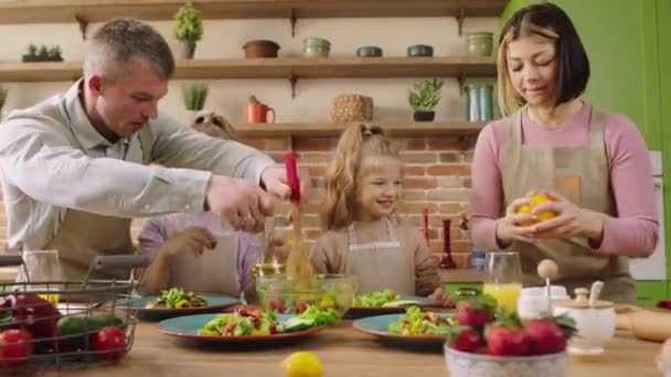 Happy family time for a young family mom dad and two cute girls preparing together healthy dinner at amazing kitchen island they smiling large and feeling excited. Shot on ARRI Alexa Mini — ストック動画