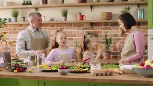Pretty two girls have a fun time with their parents at the kitchen island they eating fresh and healthy food and preparing the dinner all together — Stock Video