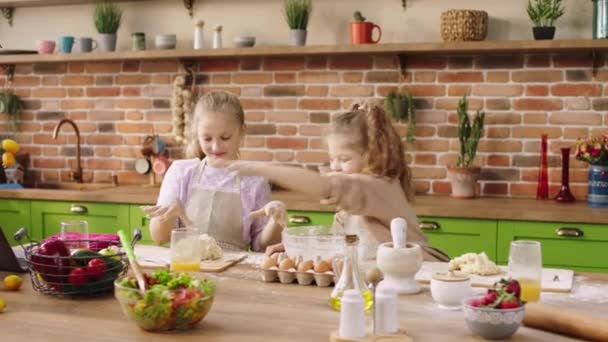 Incrível e feliz duas irmãs meninas bonitos se divertir na ilha da cozinha juntos preparando a massa para cozinhar uma deliciosa sobremesa — Vídeo de Stock