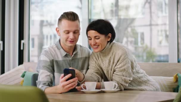 Charyzmatyczna młoda para zrobić kilka zdjęć następnie patrząc na nich ze smartfona w kawiarni — Wideo stockowe