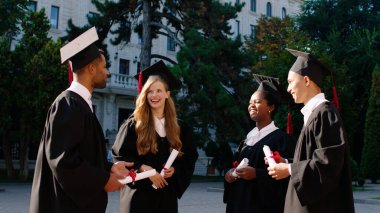 Üniversite bahçesinden mezun olan bir grup öğrenci ellerinde diplomalarıyla birlikte mutlu bir şekilde gülümseyerek ve heyecanlı bir şekilde tartıştılar.