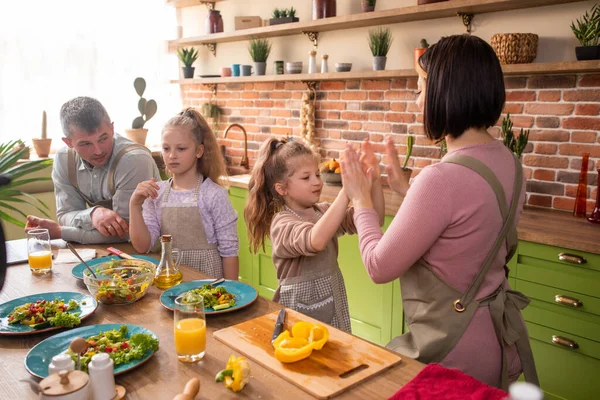 Snygga föräldrar och deras barn karismatiska två döttrar leker tillsammans på köksön medan de förbereder maten tillsammans de ler stora och glada — Stockfoto