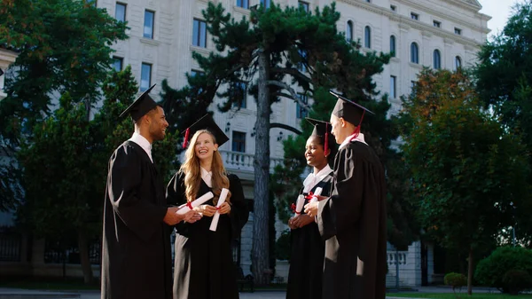 Charyzmatyczny z dużą grupą uśmiechniętych absolwentów panie i faceci rozmawiają razem po ukończeniu szkoły trzymają swoje dyplomy — Zdjęcie stockowe