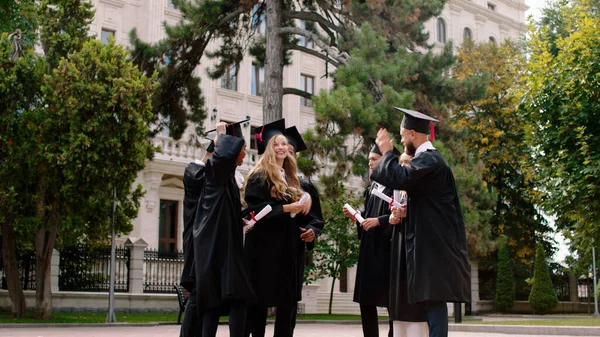 У сучасному саду коледжу група багаторасових випускників наприкінці випуску кинула випускні шапки дуже схвильованими і щасливими — стокове фото