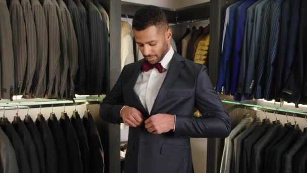 In a luxury suit shop client Afro American guy very charismatic wear a black suit and closeup the jacket he is feeling excited in a good couture suit. 4k — Vídeo de Stock