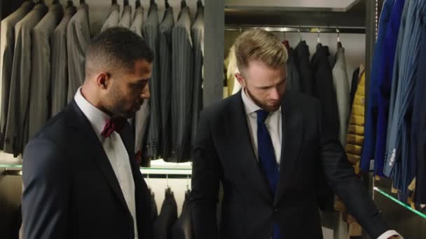 Afro American businessman at luxury suit shop have a conversation with the consultant man which are showing the new collection of casual suits to choose the most attractive one — Vídeo de Stock