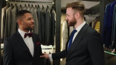 Yakışıklı Afro-Amerikalı adam lüks elbise dükkanındaki satış danışmanıyla sohbet ediyor.