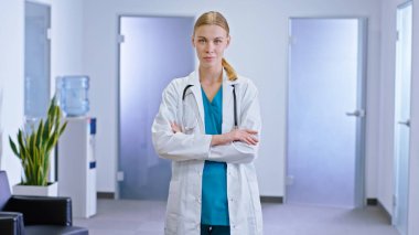 Modern hastane koridorunda kameraya bakan genç ve güzel hemşire steteskop takıp gülümsüyor.