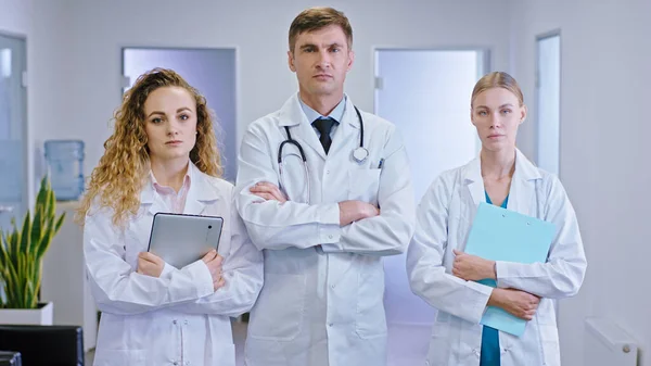 Зрелый врач и его медсестра стоят перед камерой в середине коридора больницы с цифровым планшетом и картой. — стоковое фото