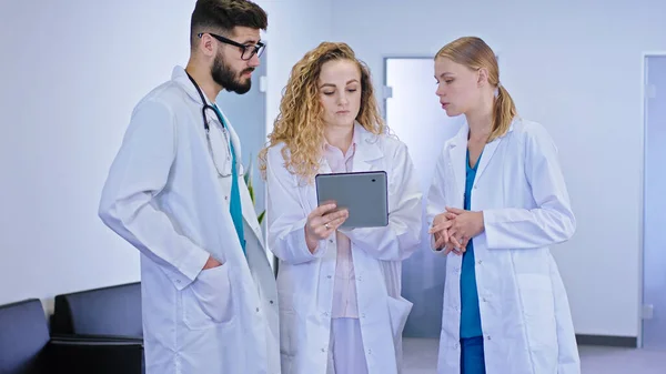 Soustředěná hlavní lékařka a sestry analyzující problém pacienta pomocí digitálního tabletu v moderní nemocniční chodbě se soustředily na diskusi — Stock fotografie