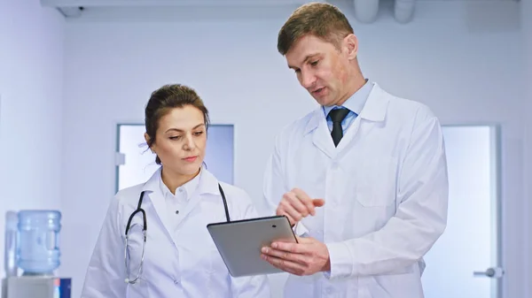V osvětlené chodbě blízko kamery muž a žena lékaři diskutují o diagnostice pacienta pomocí digitálního tabletu — Stock fotografie