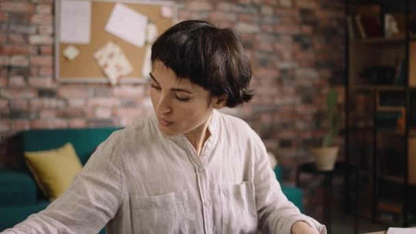 Beautiful fashion designer woman with short hair working at the tailoring atelier she take the notebook to make some notes and sketch for future collection — Stock Video