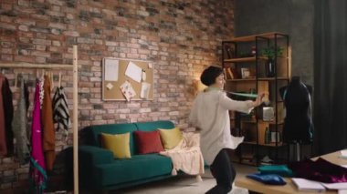 In front of the camera modern fashion office attractive clothing designer woman dancing over the sofa then jumping and feet excited while she creates new collection of clothes