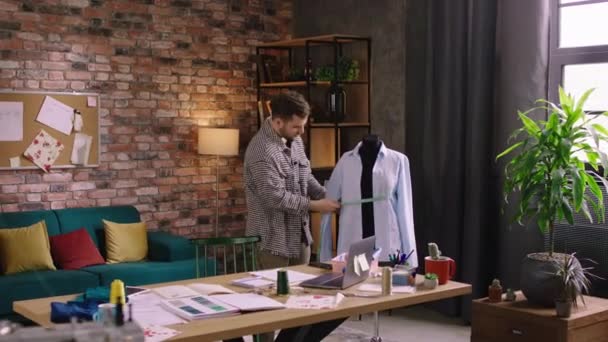 Heerlijk uitziende man, mooi gekleed doet metingen op een etalagepop en werkt heel hard als hij kleding ontwerpt — Stockvideo