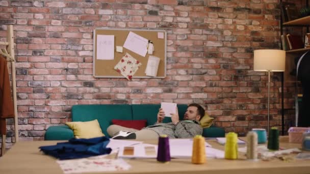 Arbetar från sin skräddarsydda ateljé modedesigner lägga sig på soffan och göra några anteckningar på sin bärbara dator om den nya kollektionen. Skjuten på ARRI Alexa Mini — Stockvideo