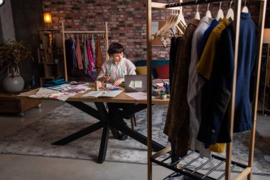 Moda tasarımcısı kadın. Çok yaratıcı. Kağıdında yeni kıyafetler tasarlıyor. Sonra da bilgisayarı kullanarak küçük işletme atölyesi tasarımı konsepti üzerinde çalışıyor.