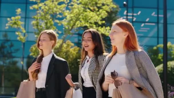 Moderne Bauarchitektur in der Mitte der Stadt schöne lächelnde große Gruppe von Frauen nach einem guten Einkaufstag glücklich nach Hause gehen mit ein paar Öko-Einkaufstüten und diskutieren alle zusammen — Stockvideo