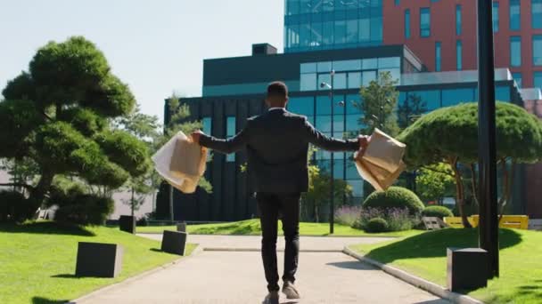 Black business man in the suit going to his working to the main business centre he holding some shopping bags he jumped excited taking video from the back — Video