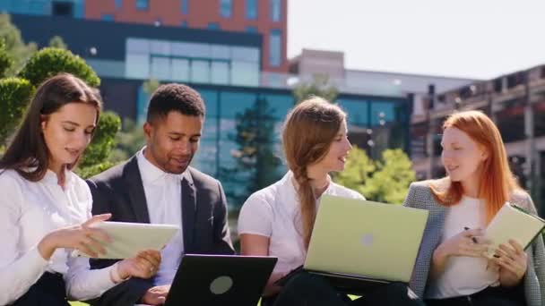 Good looking young office team working together on the laptops and tablets in the middle of business centre park they discussing and feeling great. 4k — Video