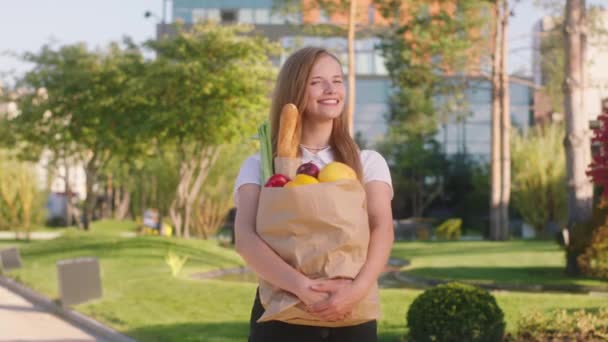 Beautiful woman posing in front of the camera she holding eco bag full of food in the middle of modern street — Vídeo de Stock