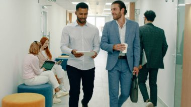 Ofiste çok yoğun bir gün, iki çalışan takım elbiseli adam koridorlarda yürüyor ve elinde bir tabletle konuşuyorlardı, bir sürü farklı insanın yanından geçiyorlardı.
