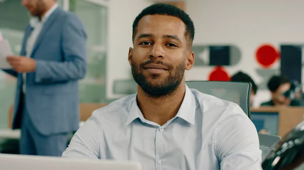 A handsome black man with a nice haircut and a beard is sitting at the office at his desk and doing work, looking very serious