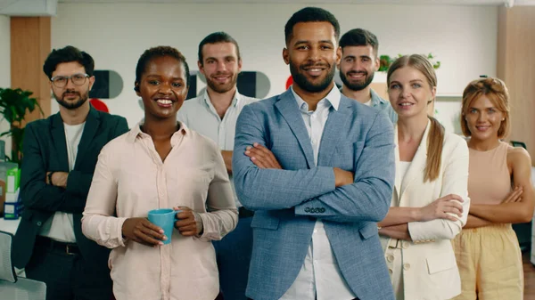 Un grupo de gerentes y asistentes que trabajan duro están de pie en una gran oficina actual y sonriendo ampliamente mientras cruzan sus brazos. —  Fotos de Stock