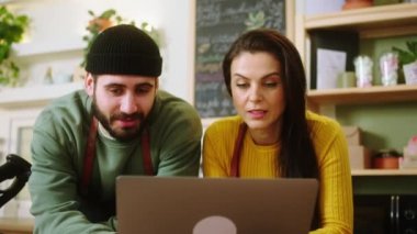 Modern kahve dükkanında, kafe kadının sahibi ve genç baristanın müşterilerden online siparişleri almak için dizüstü bilgisayarı kullanması. v