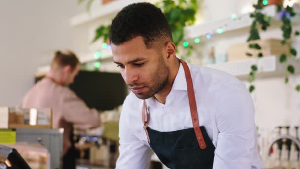 Afroamerikanischer Barista-Mann in einer gemütlichen Café-Bar, der zusammen mit seinem Kollegen Barista-Mann ein paar Online-Bestellungen auf dem Laptop eintippt — Stockvideo