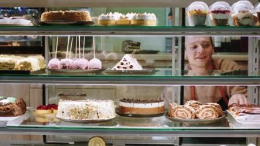 In front of the camera at the coffee bar good looking young guy salesman open the showcase fridge and take some deserts to selling for customer