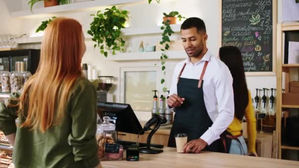 Афро-американський бариста дає чашку кави і вводить замовлення на термінал леді-клієнтка взяти кредитну картку, щоб зробити передачу в кафе бар — стокове відео