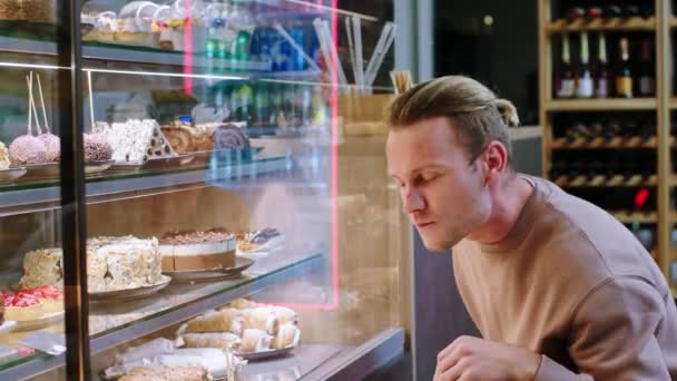 Happy and charismatic guy customer chooses some fresh dessert from the showcase fridge in the bakery cafe — Stok video