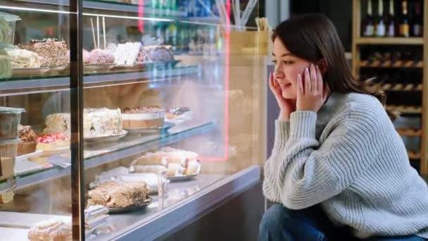 At the cozy coffee shop happy lady very hungry looking at the showcase fridge to choose her favourite dessert — Stok video