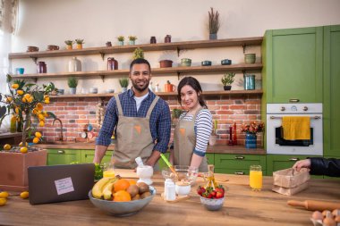 Modern mutfakta karı koca birlikte güzel vakit geçirirken kocası mutfak adasında dizüstü bilgisayarla yemek pişiriyor ve bulaşıkları yıkıyor.