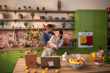 Birlikte yemek hazırlarken mutlu ve heyecanlı bir çift mutfak adasında dans ediyor ve büyük bir gülümsemeyle anın tadını çıkarıyor.