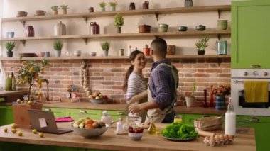 In the kitchen happy and beautiful couple multiracial dancing while preparing the dinner together they singing and enjoy the moment together