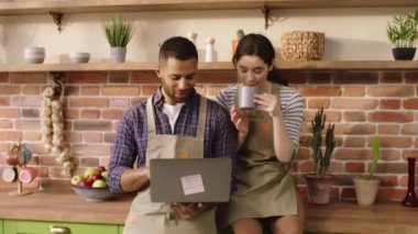 Happy couple very excited in the morning Afro American man holding his laptop together with his partner woman looking over the laptop while female drinking her coffee in the kitchen